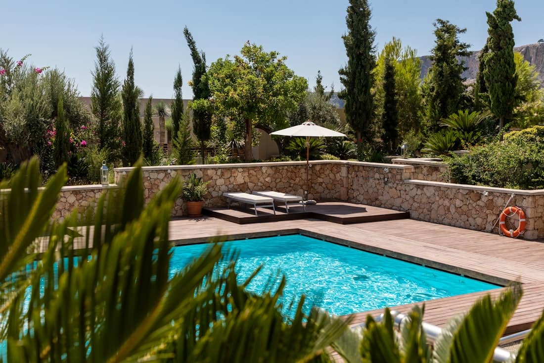 Free-form swimming pool with a stone deck and lounge area surrounded by landscaping